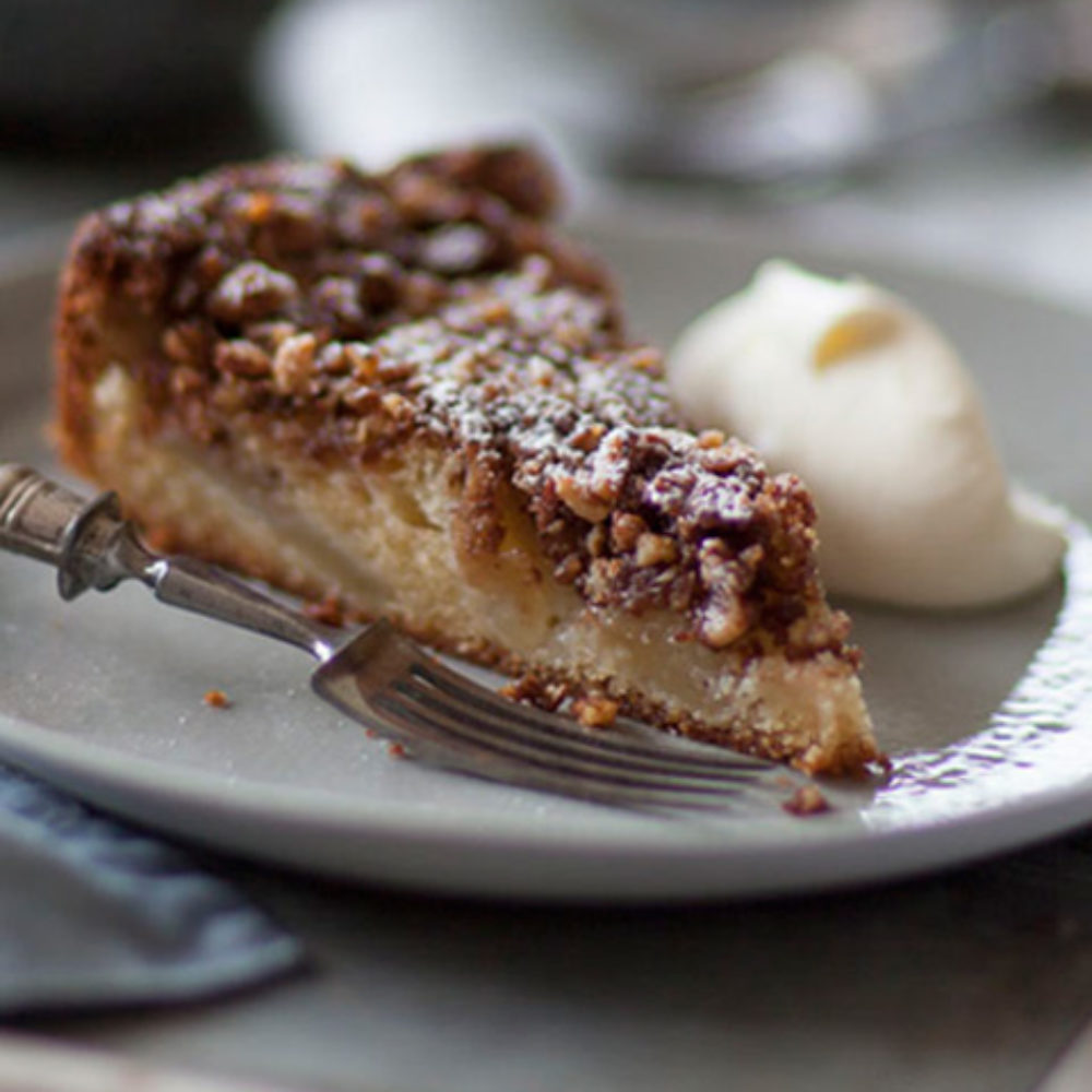Slice of crumb-topped cake dusted with powdered sugar on a gray plate, with a fork beside it. A scoop of pale ice cream or cream sits on the plate in the background.