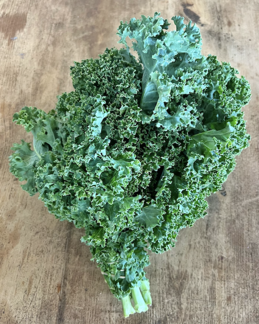 Overhead view of a large bunch of curly green kale with stems attached, placed on a wooden tabletop.
