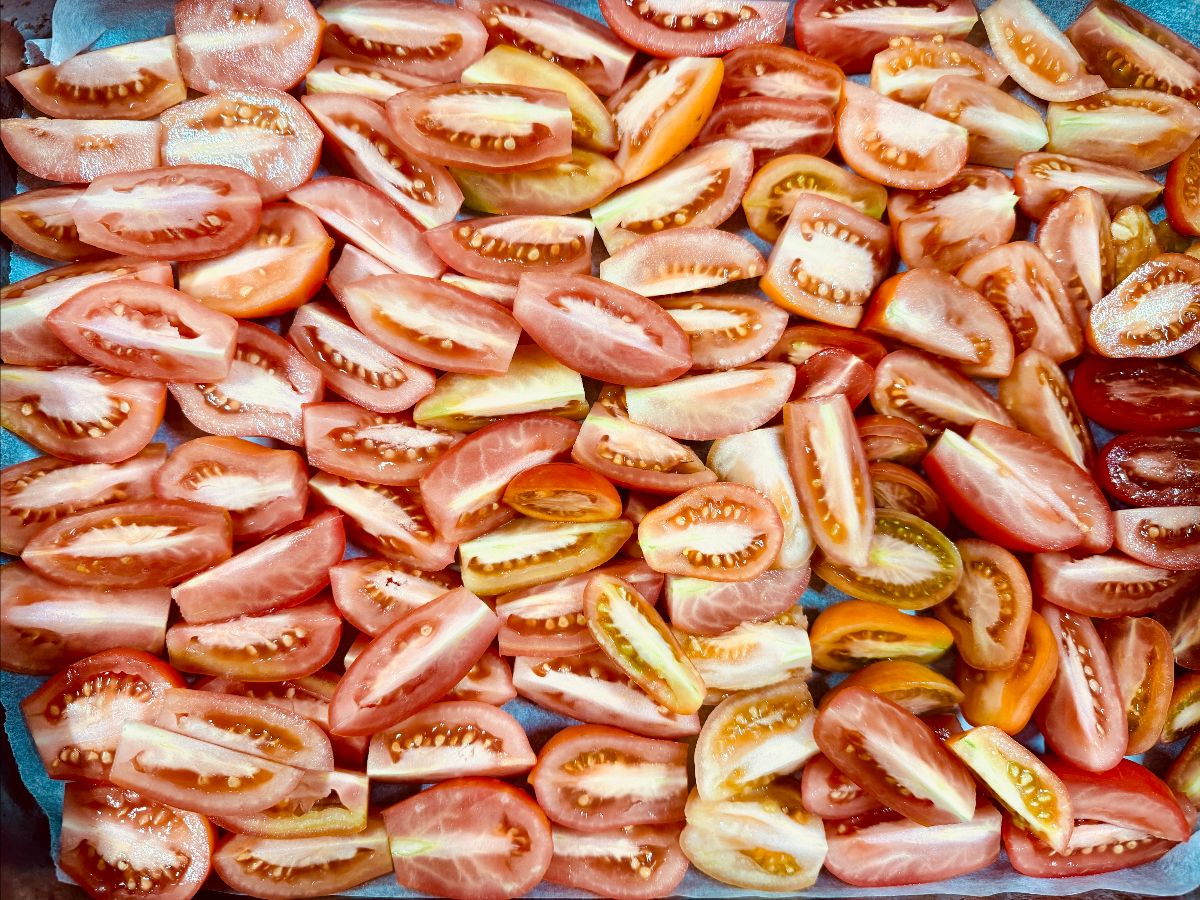 Close-up of many tomato wedges in red, pink, and yellow tones spread across a parchment-lined tray. The cut tomatoes fill the frame in an overhead view.
