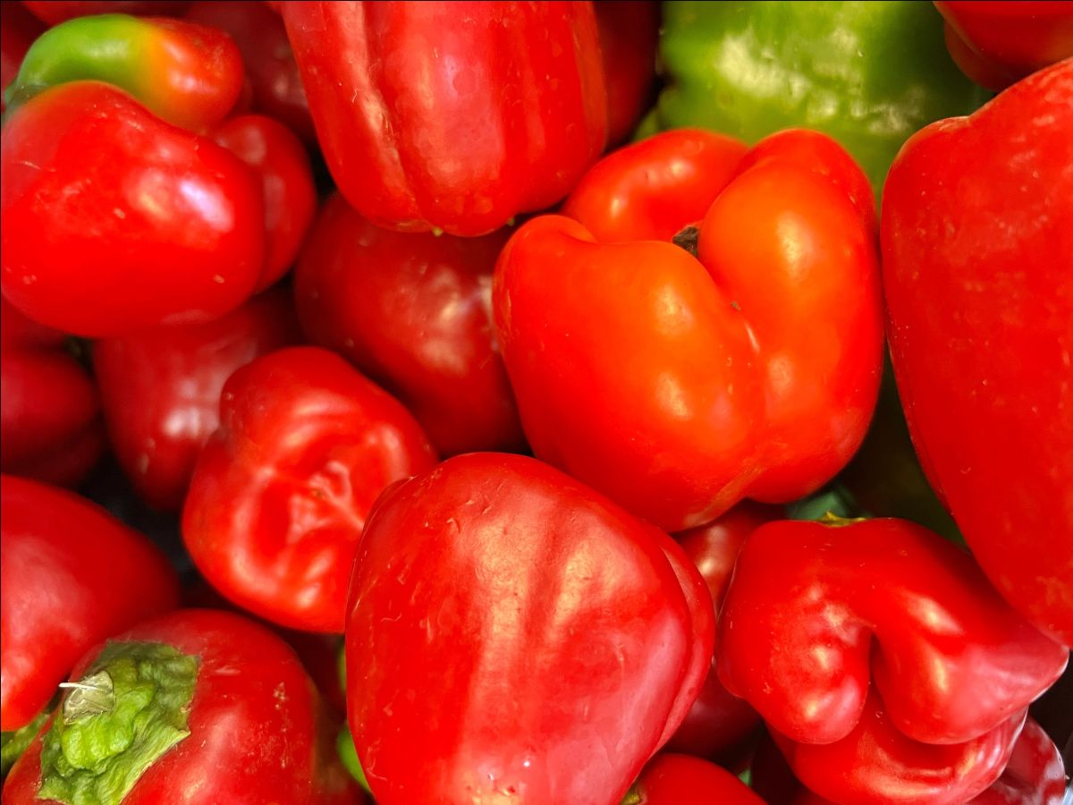 Close-up of a pile of red bell peppers with a few green peppers mixed in. The peppers fill the frame.