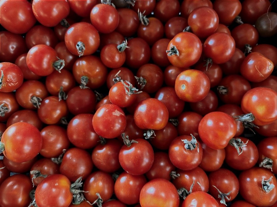 Close-up of a pile of small red cherry tomatoes with green stems attached, filling the frame