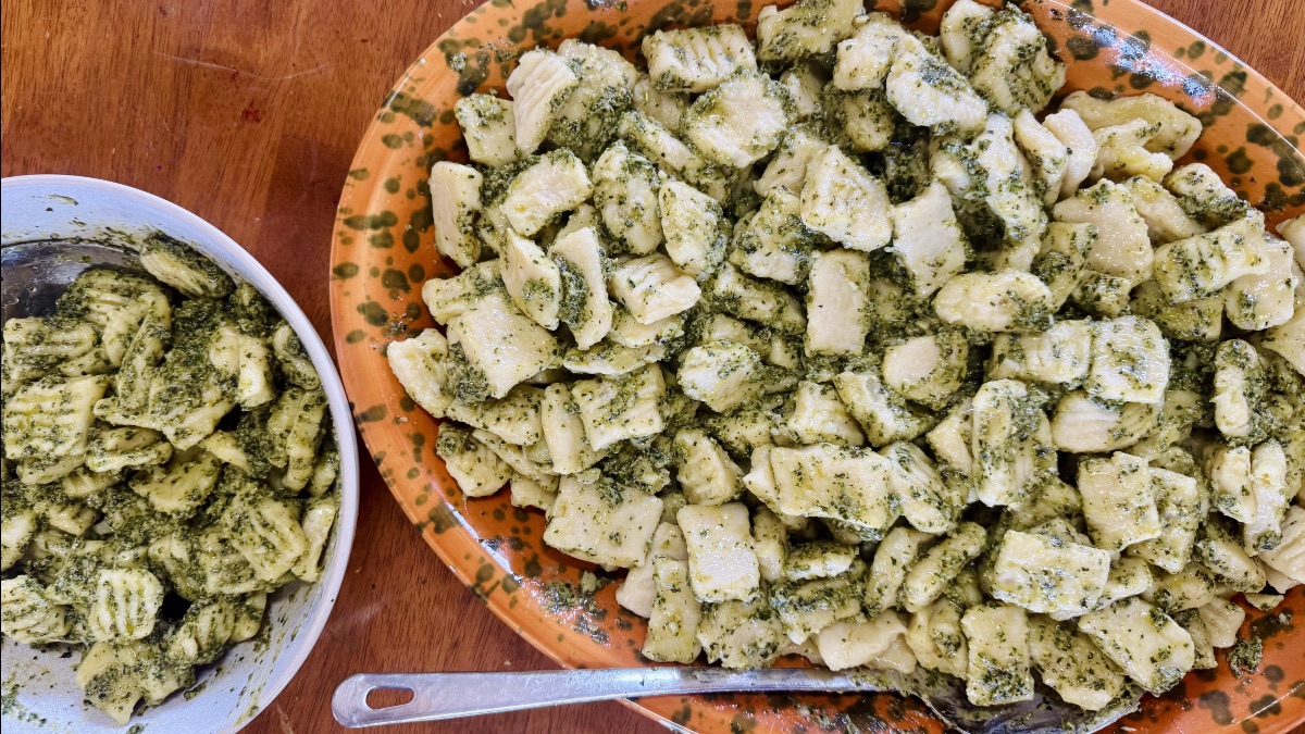 A large spotted ceramic platter and a bowl heaped with homemade pesto gnocchi on a wooden table