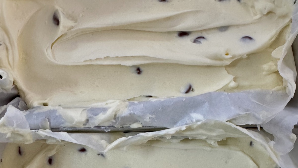 Close-up of homemade no-churn vanilla and choc chip ice cream in baking paper-lined trays with a smooth creamy texture and chocolate chips throughout